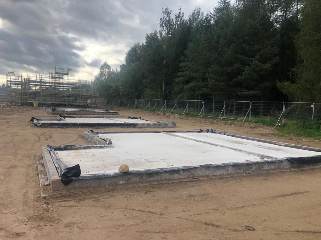 Insulated slab foundations laid out across the site, with the frames of earlier homes visible beyond