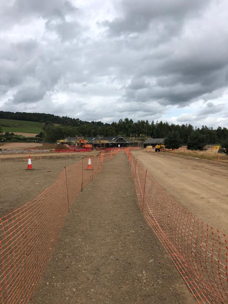 A wide view of the Perthshire site, showing the haul road, site fencing and the estate under construction against wooded hills